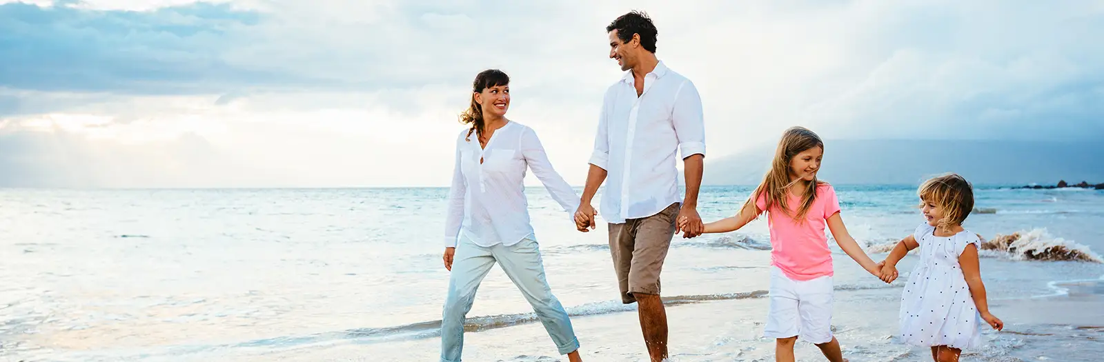 Happy couple with two daughter walking on the beach.